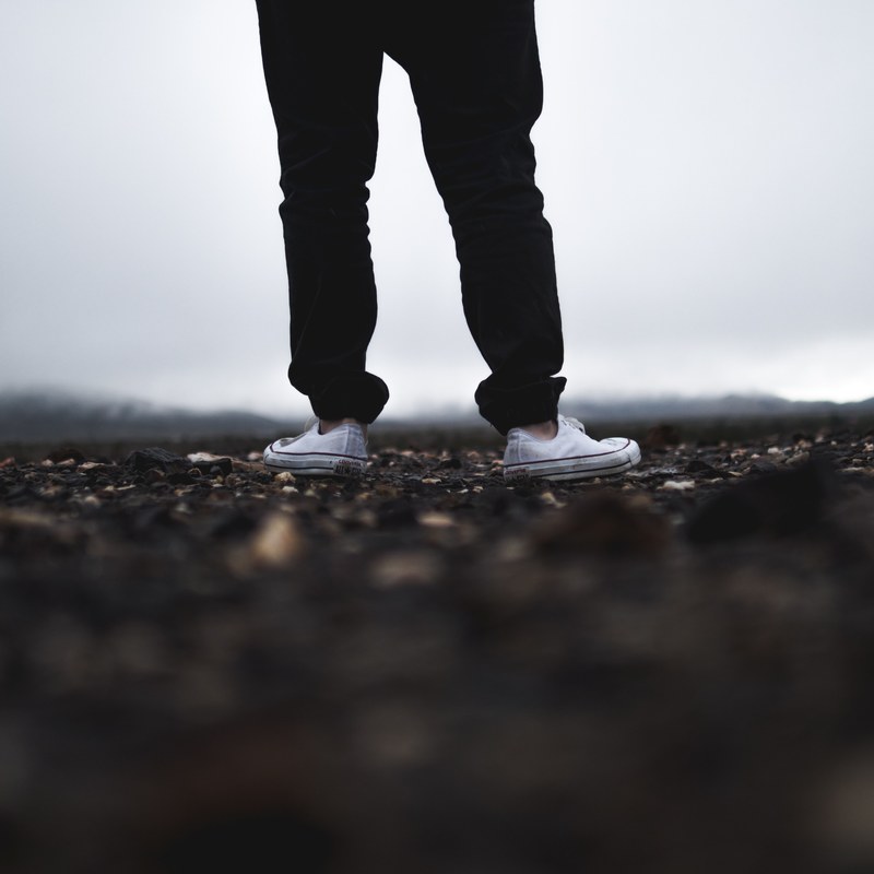 low shot of person in converse sneakers standing on rocky ground, standing on the shore 4k