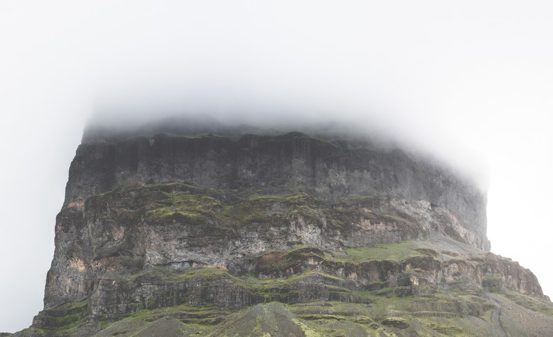 the base of a mossy rock tower with its top shrouded in thick fog, foggy rock tower 4k