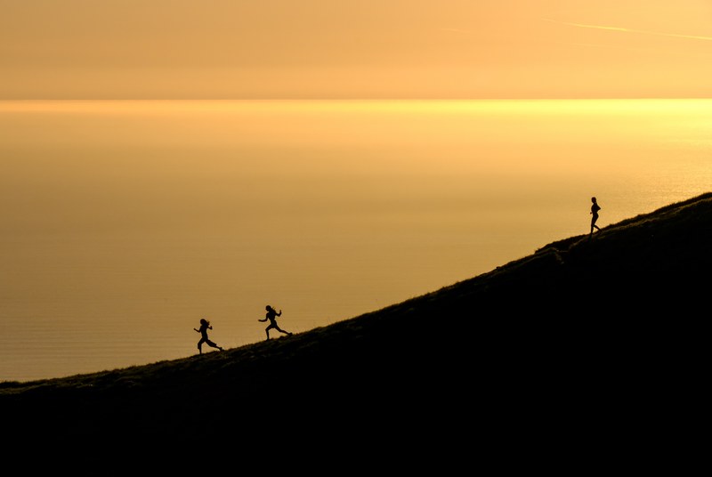 three women energetically running down mount tamalpais as waters in the distance reflect the golden sunset, running down mount tamalpais in gold 4k