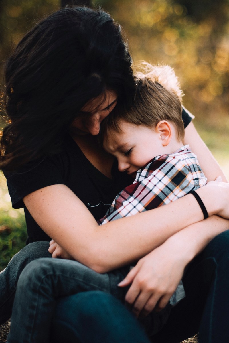 a brunette mom affectionately cuddling her young toddler son who is sat on her knees, a cuddle from mom 4k