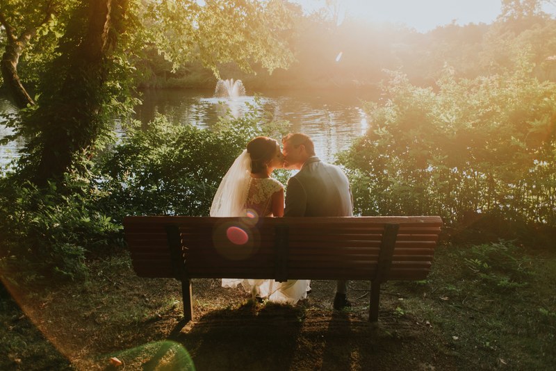 romantic sunlight over a just married couple kissing on a park bench at a lake, bench at the lake 4k