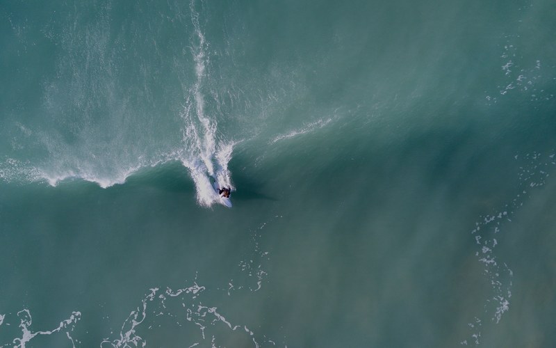 a drone shot of a surfer riding a wave in gisborne new zealand, super woman 4k