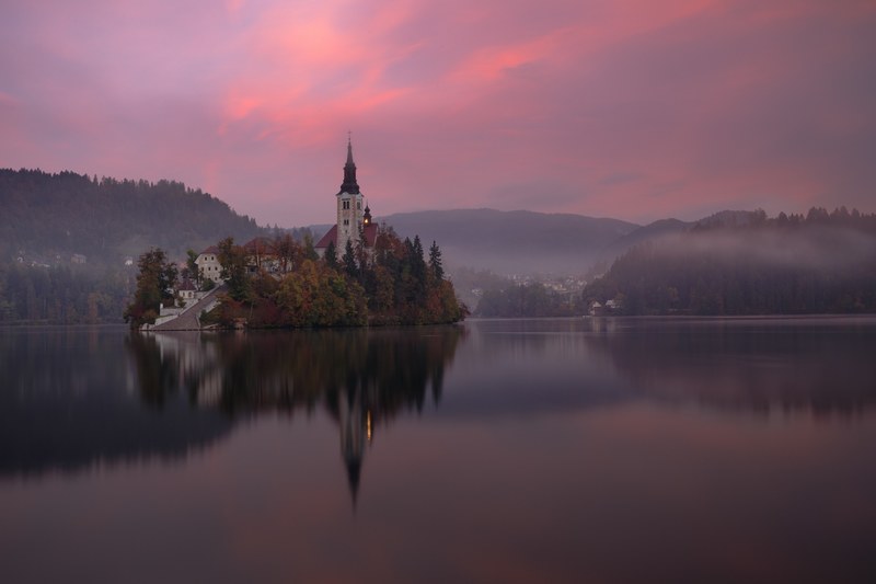a village church and its foggy sunset scenery are reflected upon the waters of lake bled in slovenia, foggy sunset at lake bled 4k