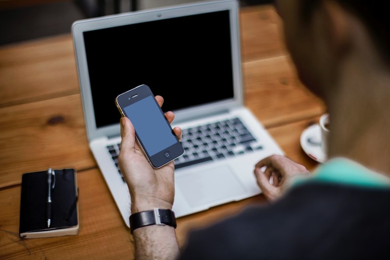 a man holding an iphone while sitting at a desk with a laptop, man with smartphone and laptop 4k