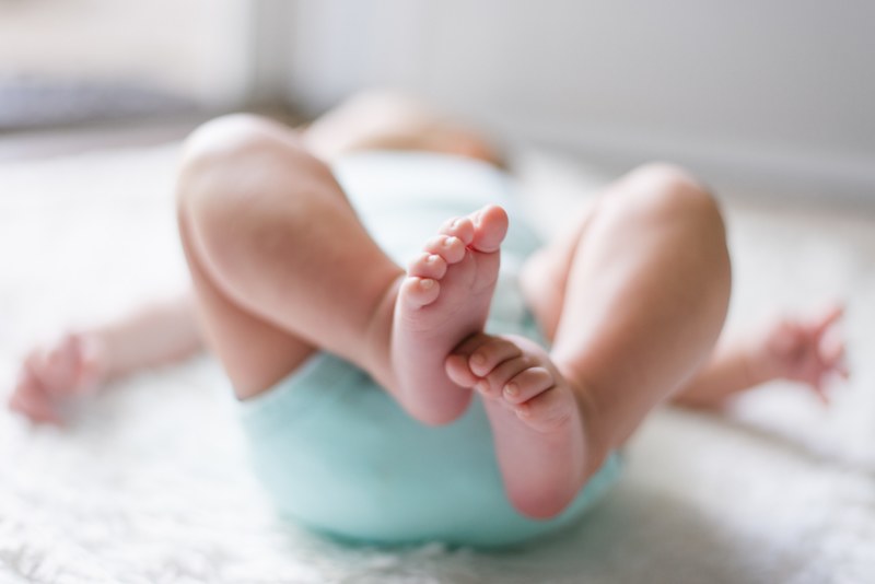 baby wiggles their toes and lies on their back in a blue onesie, tiny feet 4k