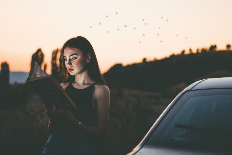 young long hair woman reading a book by the car on a sunset in the nature, dream travel 4k