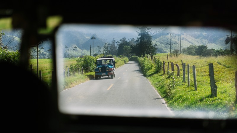 a close up of a rear view mirror with a car driving on a rural road among green hills, green rear view mirror 4k