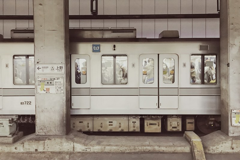 white subway car with doors and windows stopped at ueno station in between two concrete columns, 4k