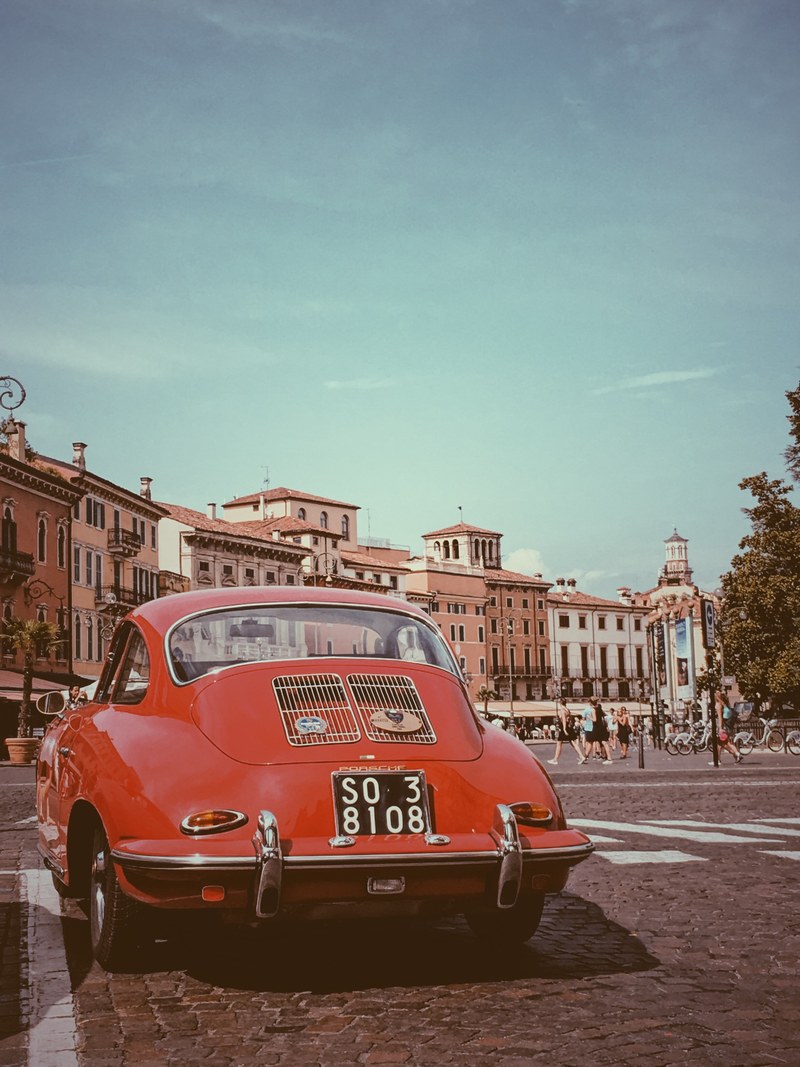 classic red porsche in the street in front of a town square and people walking in the street, porsche verona 4k