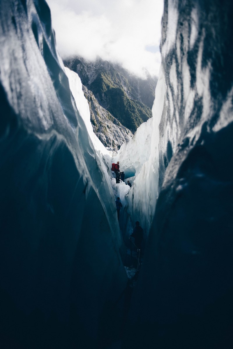 several hikers exploring a glacial crevasse in the mountains, between walls of ice 4k