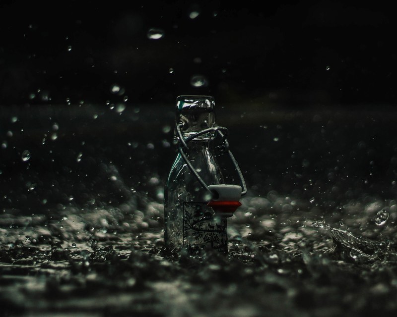 glass bottle collects rain as water splashes around it, water in a bottle 4k