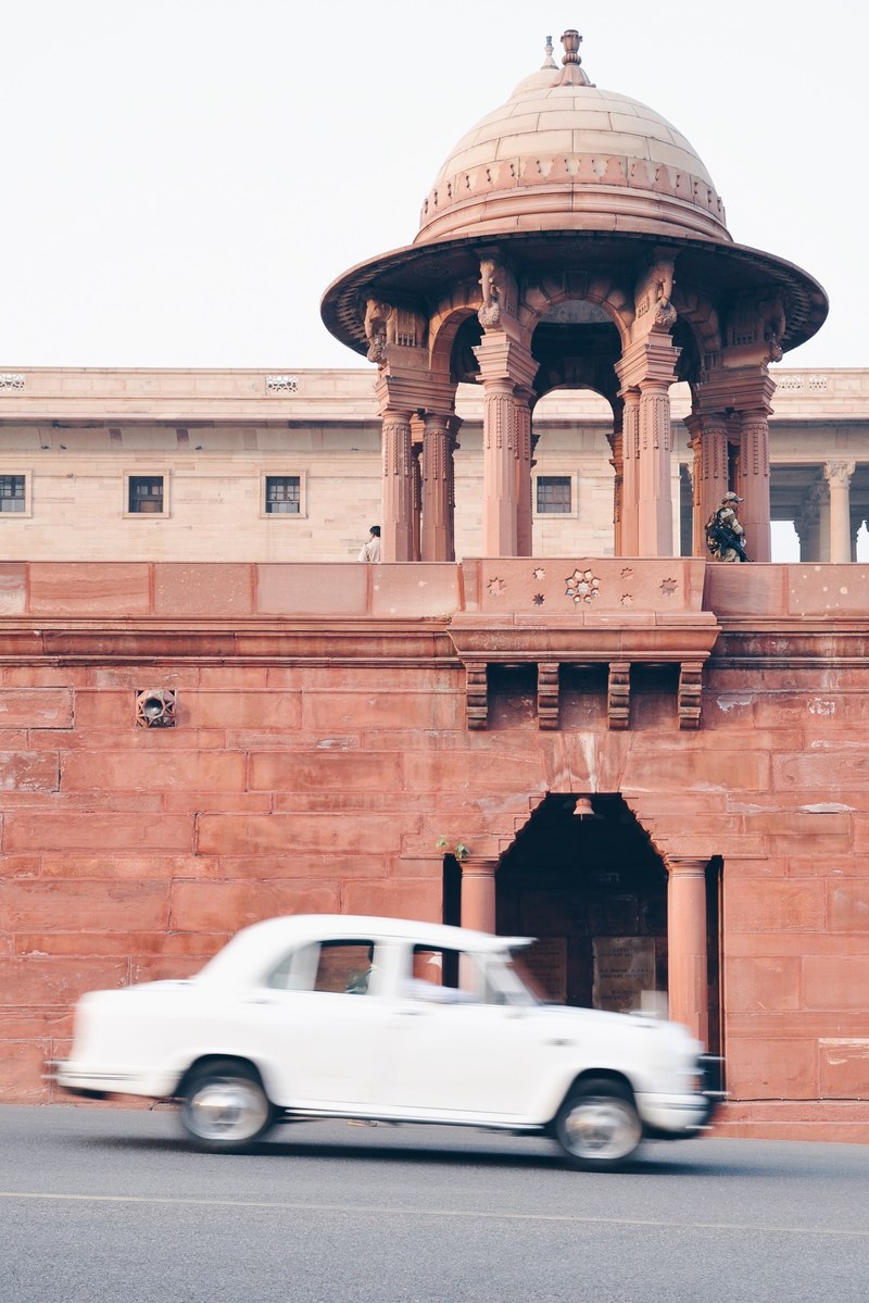 white car driving past old stone wall in delhi, first day in delhi 4k