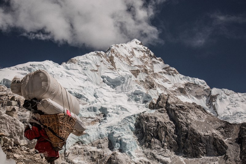 a climber carrying a basket with load trekking on snow in nepal, up up up 4k