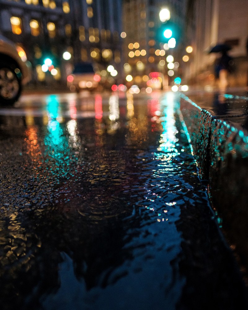a night time image capturing the rain on the ground on a downtown street, _flooded downtown street 4k