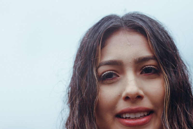a woman with long brown wet hair and dripping forehead smiles against a blue background, woman with wet hair 4k