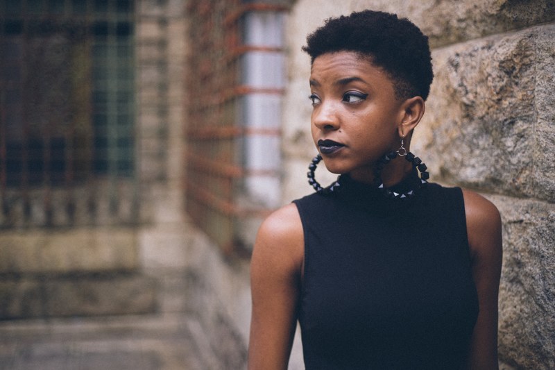 woman wearing large hoop earrings and a black sleeveless shirt near a stone wall, chic and glamorous 4k
