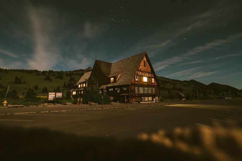large cabin like house lit up from the inside at dusk in a field with mountains in the background, night sky hotel 4k