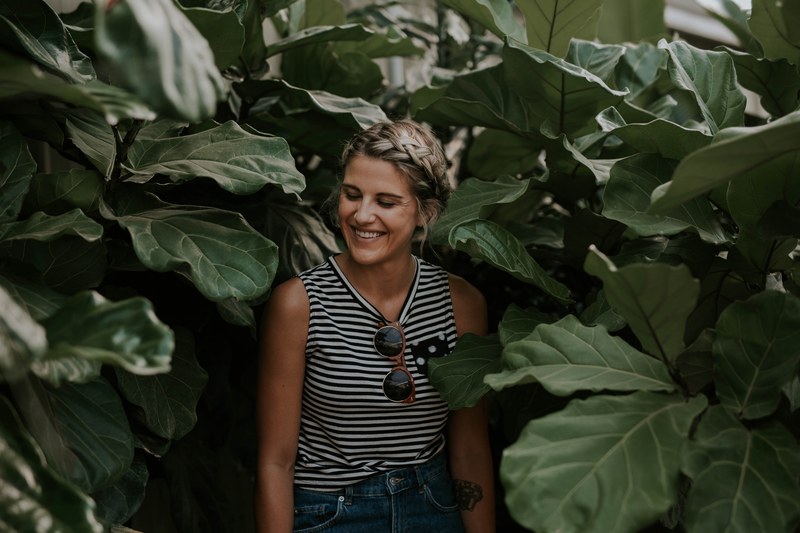 a woman in a tank top smiles with her eyes closed standing among foliage, woman smiling among foliage 4k