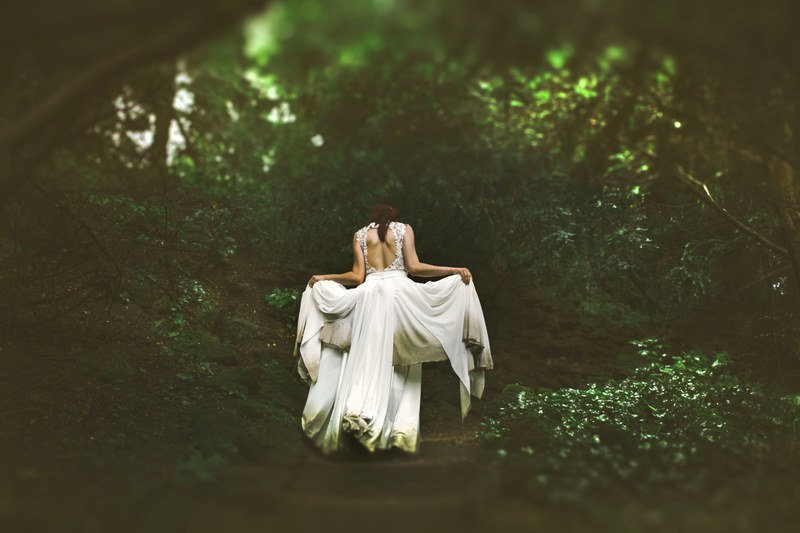 a woman lifting up the ends of her white wedding dress on a forest path, forest bride in flowing dress 4k