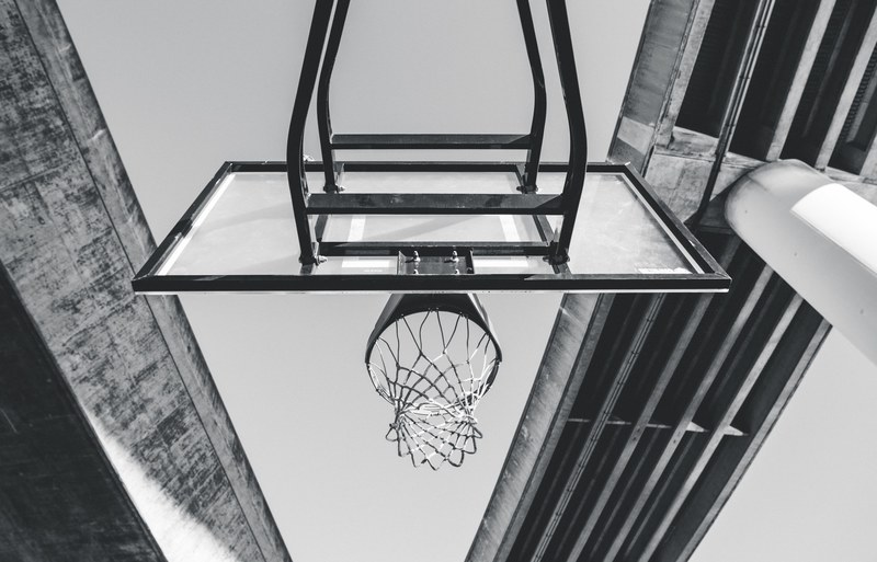 a black and white photo from beneath an outdoor basketball net on a court under a large overpass bridge, basketball under the overpass 4k