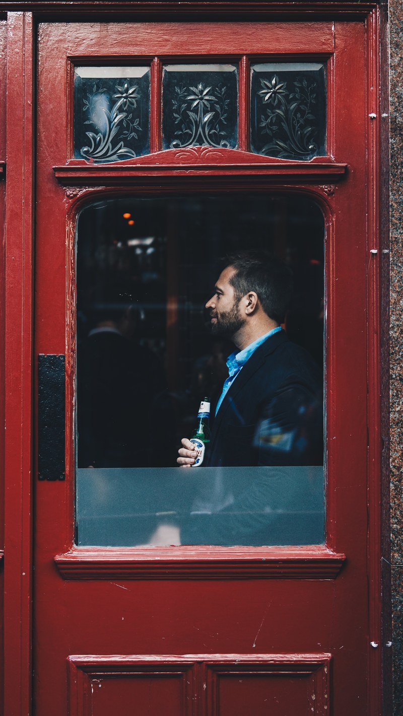 a man holding a beer and standing at the window of a red door in china town, beer brings happiness 4k