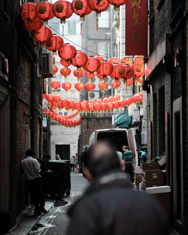 a man looks down an alleyway with strings of paper lanterns hung from the buildings, chinatown 4k