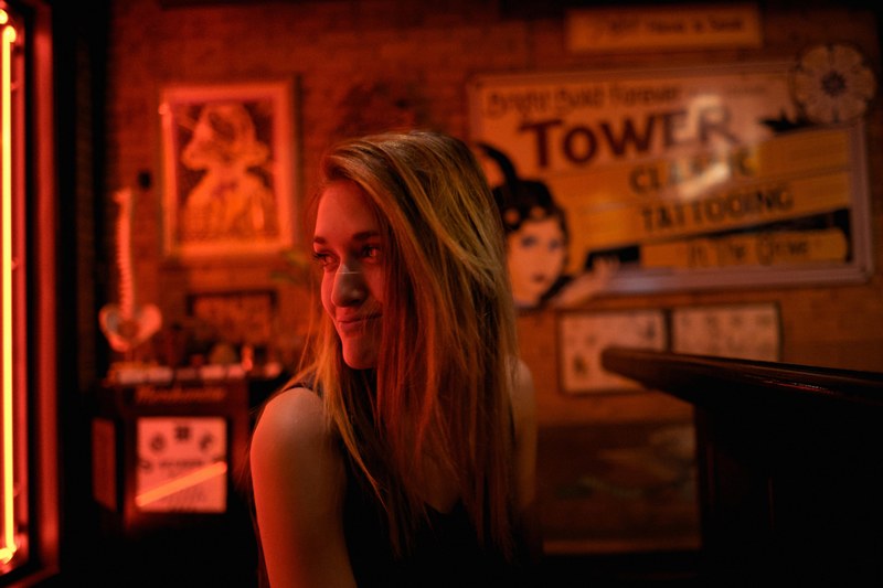 a woman in a bar lit in red smiles mischievously over her shoulder, first tattoo 4k