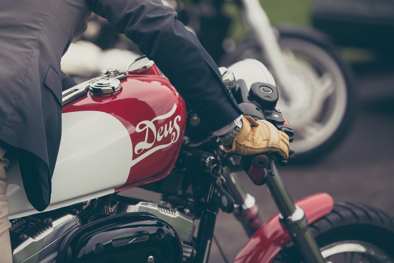 a man wearing a suit and gloves riding a red and white deus motorcycle at the university of sydney, deus motorcycle 4k