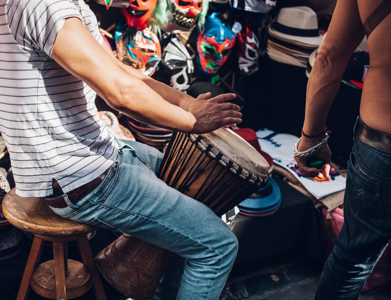 a man in jeans and t shirt playing a tall drum on brick lane market, drummer on brick lane market 4k