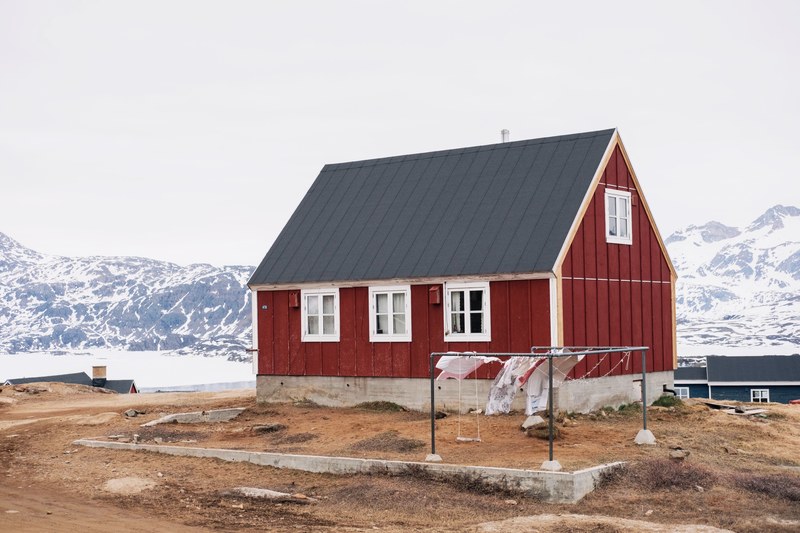 red house with laundry drying outside and snow capped mountains in the background, house in tasiilaq 4k