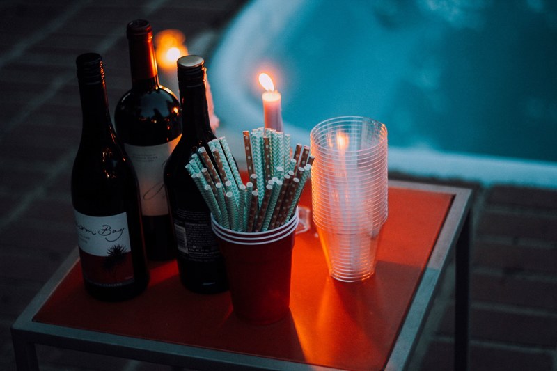 a tabletop containing wine straws candles with flames and plastic cups by a pool in redding, wine in the hot tub 4k