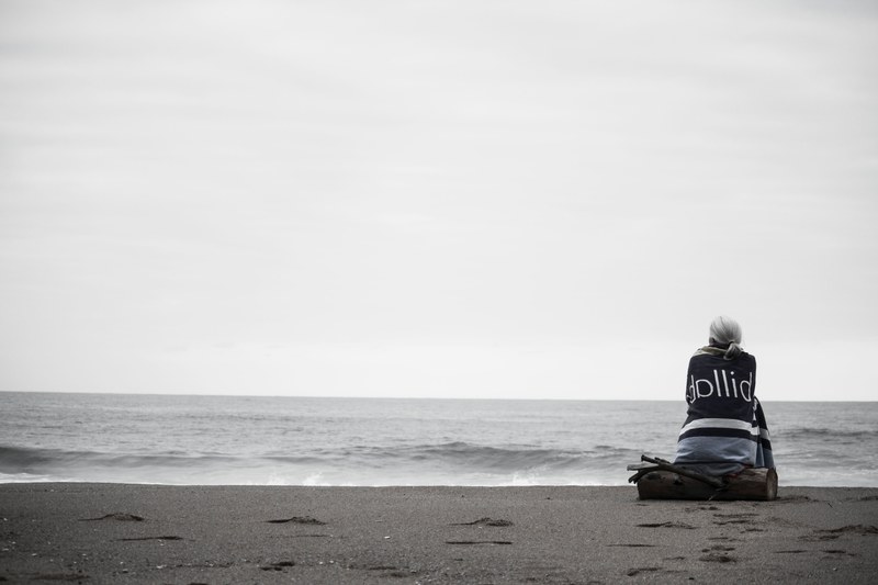 black and white shot of a woman sitting alone in the seashore watching the still ocean, lonely woman at beach 4k