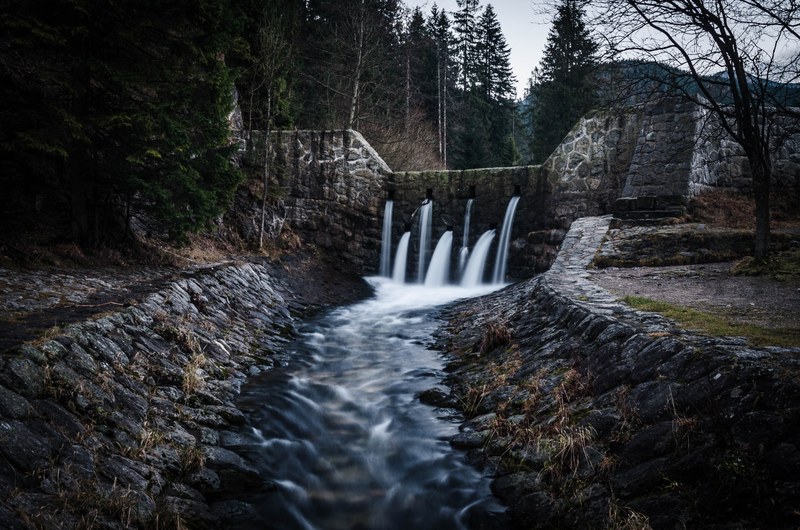 a stream flowing through several openings in a stone bridge, water flowing through a bridge 4k