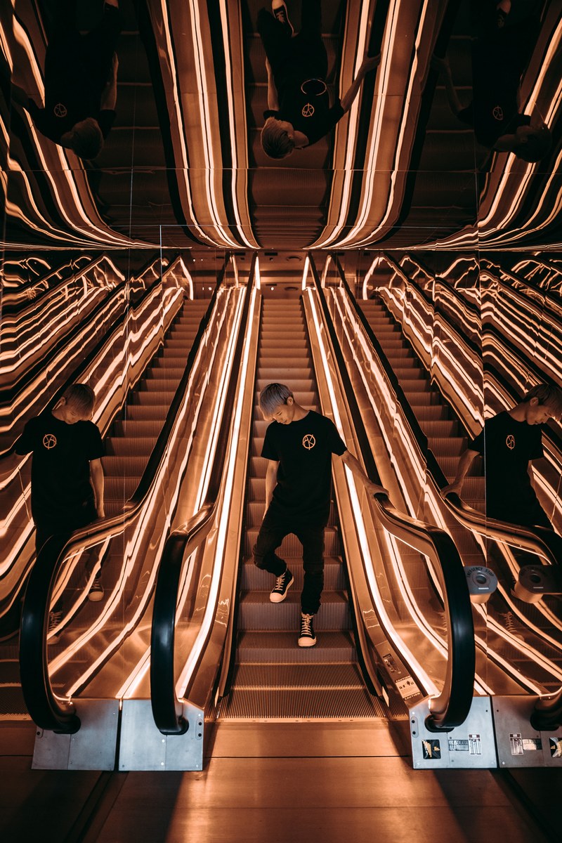 a man wearing all black reflects in two mirrors as he rides an escalator while looking down, _being single seeing double making triple 4k