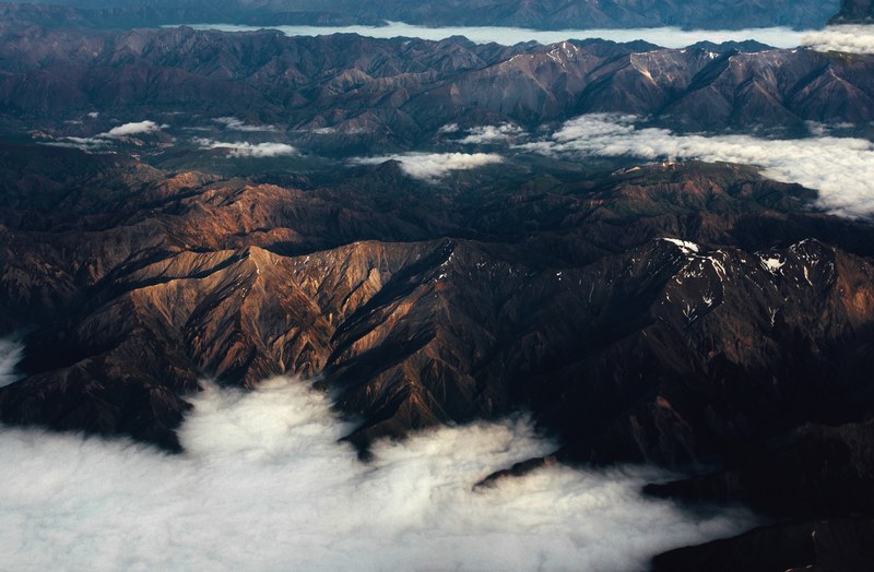 an aerial shot of clouds gathering in the valleys between folded mountains in new zealand, ranges 4k