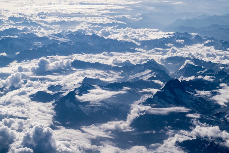 an aerial shot of sharp mountain ridges emerging from a sea of clouds, birds eye view of tall mountains 4k