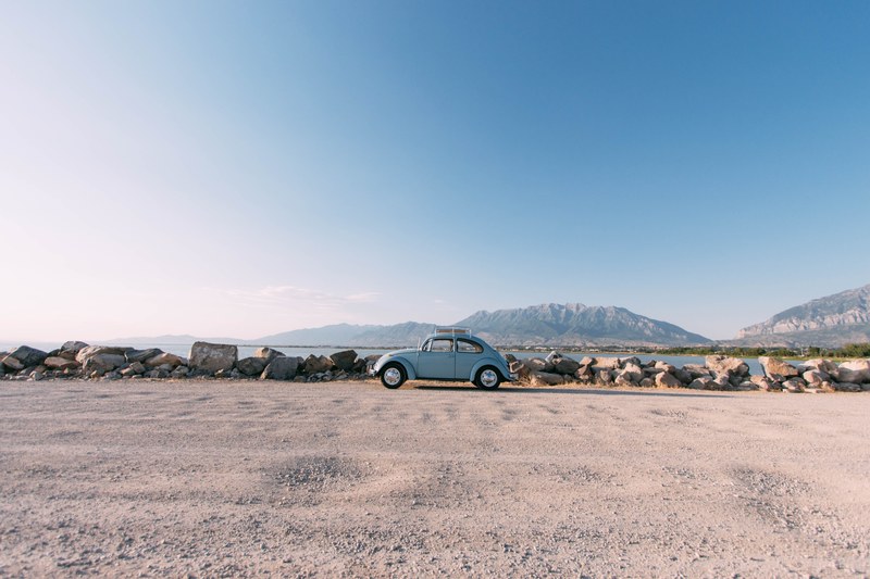vintage blue volkswagen beetle parked on road in front of lake with mountains in the distance, blue volkswagen beetle lake 4k
