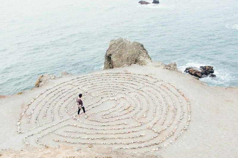 a person walking through a maze made out of rocks by the side of the beach, rock maze 4k