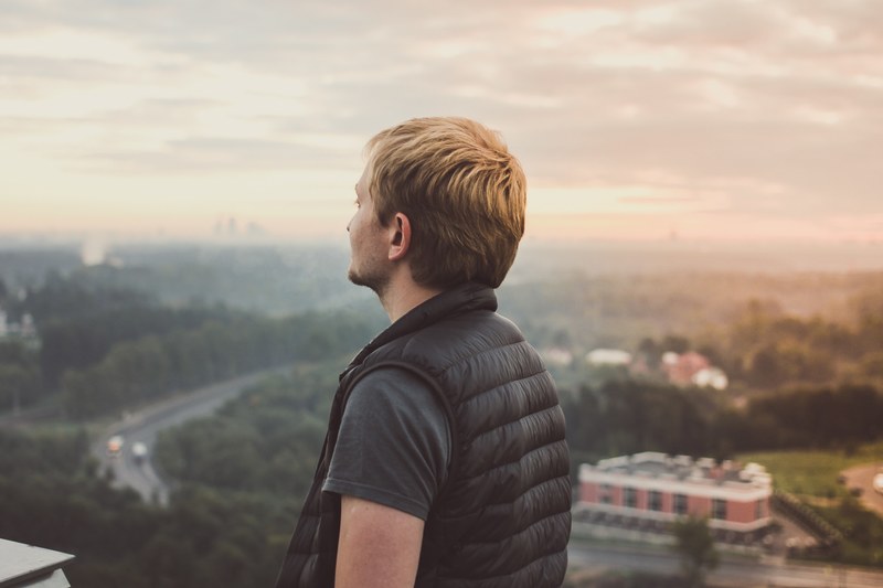 a man in a vest looking into the distance over a landscape of trees and buildings, man in down vest on overlook 4k