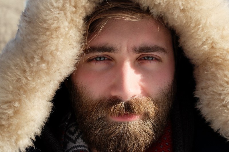 a bearded man in a furry hood with a serious expression squints his eyes, serious man in furry hood 4k