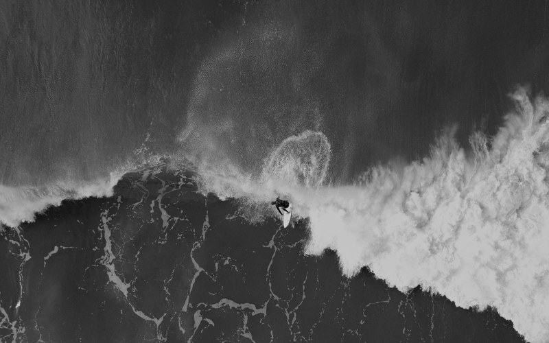 an overhead drone shot of a surfer in the foaming sea at gisborne new zealand, spray 4k