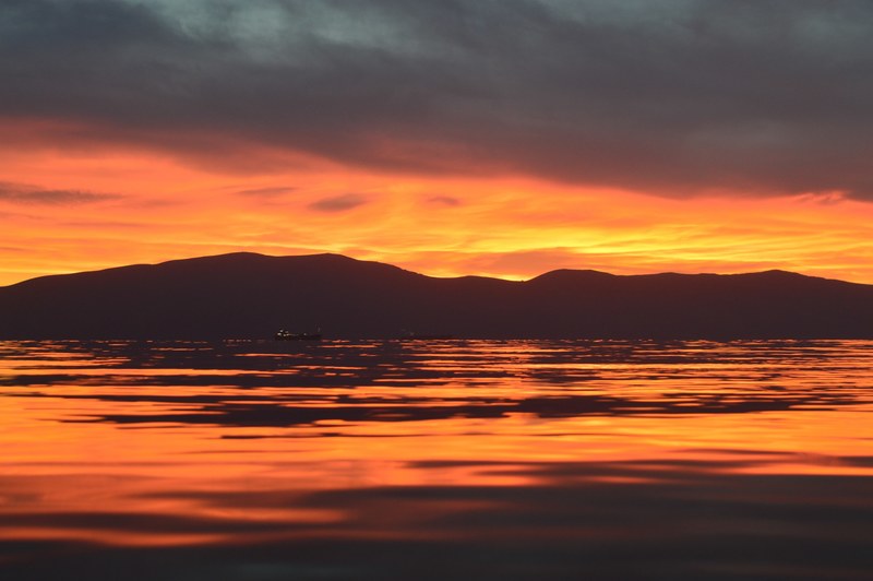 rippling water level view of orange sunrise or sunset horizon with silhouette hill in vlor, sunset in sea 4k