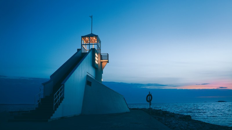 a lighthouse beacon with illuminated lights in front of a blue sky and sea at sunset oulu, night before the arrival 4k