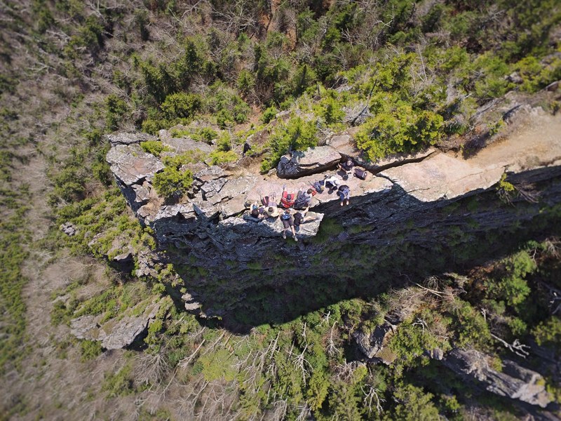 a drone shot of a group of people resting on a rocky ledge in a forest, resting hikers from above 4k