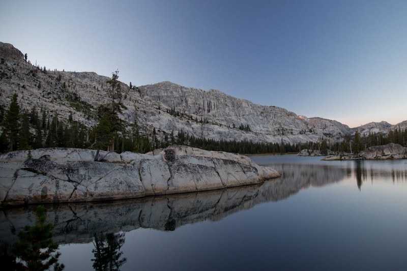 a lake during sunrise showing the reflection of rocks and trees surrounding it, still waters by the mountains 4k