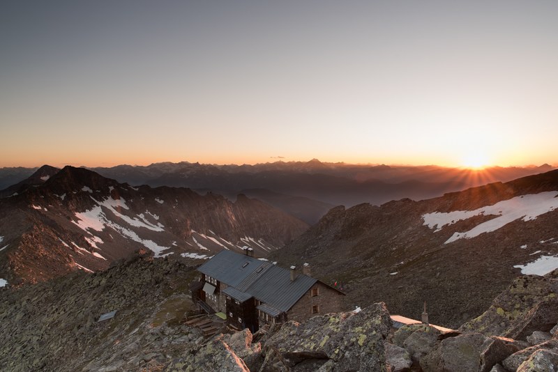 sun setting overlooking a house surrounded by snow covered mountain tops, _sunset with house on snow covered mountain 4k