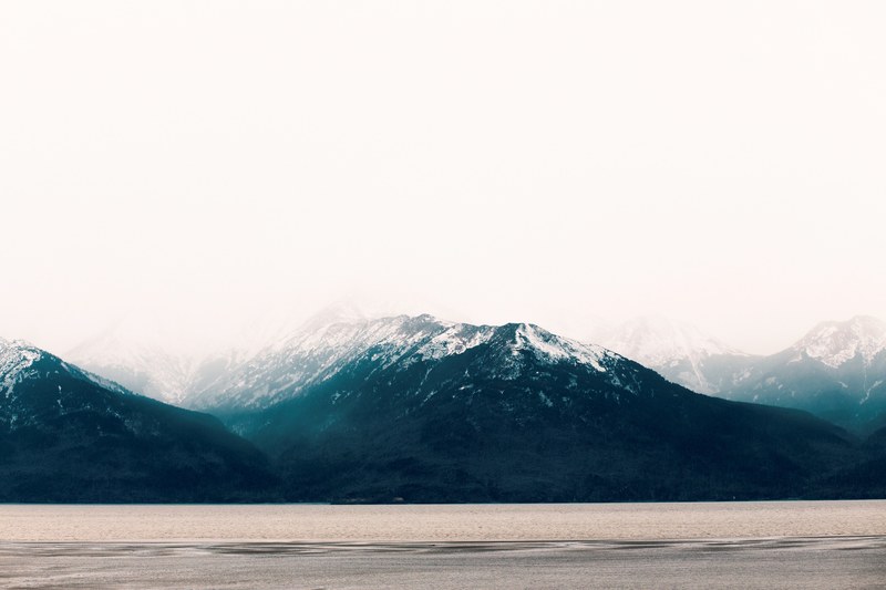 clouds enveloping the peaks of a mountain over a brown hued lake, turquoise mountains 4k