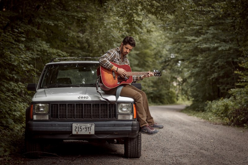 musician sitting atop his jeep playing guitar on a country road, 94 cherokee 4k