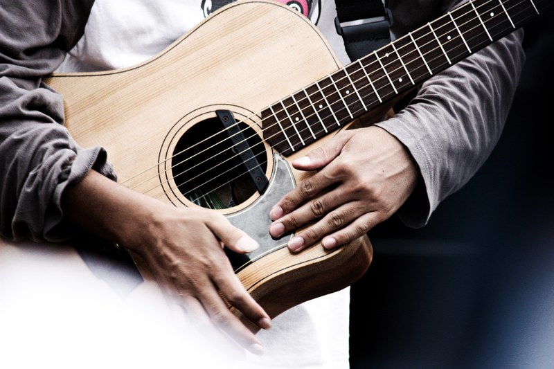 person holds acoustic guitar with strap with both hands, street musician performing with an acoustic guitar 4k