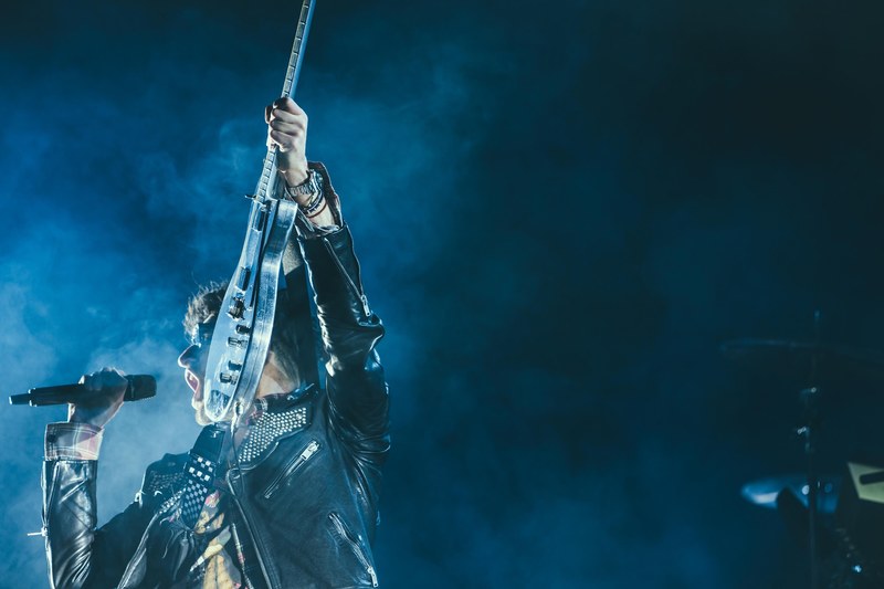 a man in a leather jacket holds up an electric guitar and shouts into the microphone, rockstar in the night_ 4k